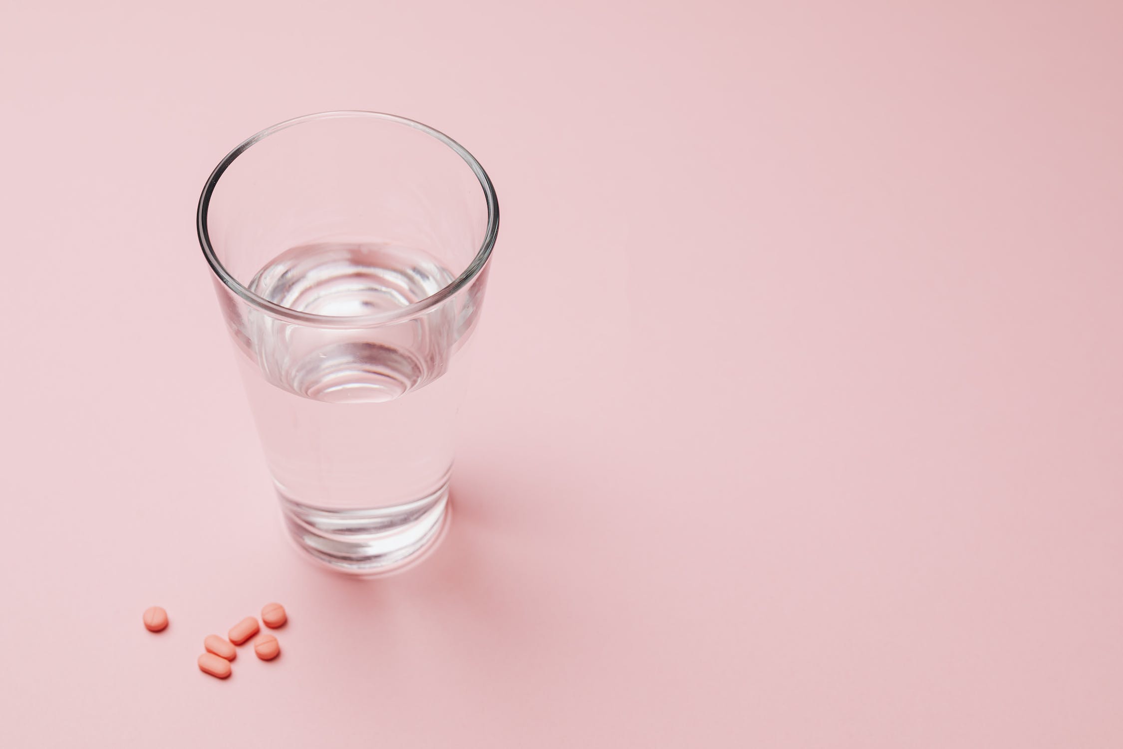Glass of water and pills on pink background